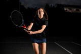 portrait of confident young woman playing tennis with tennis racket. Dark background