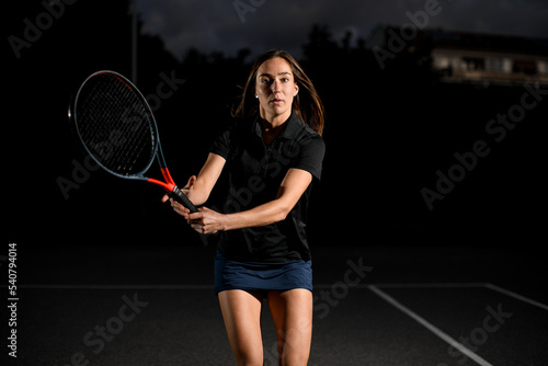 portrait of confident young woman playing tennis with tennis racket. Dark background © fesenko