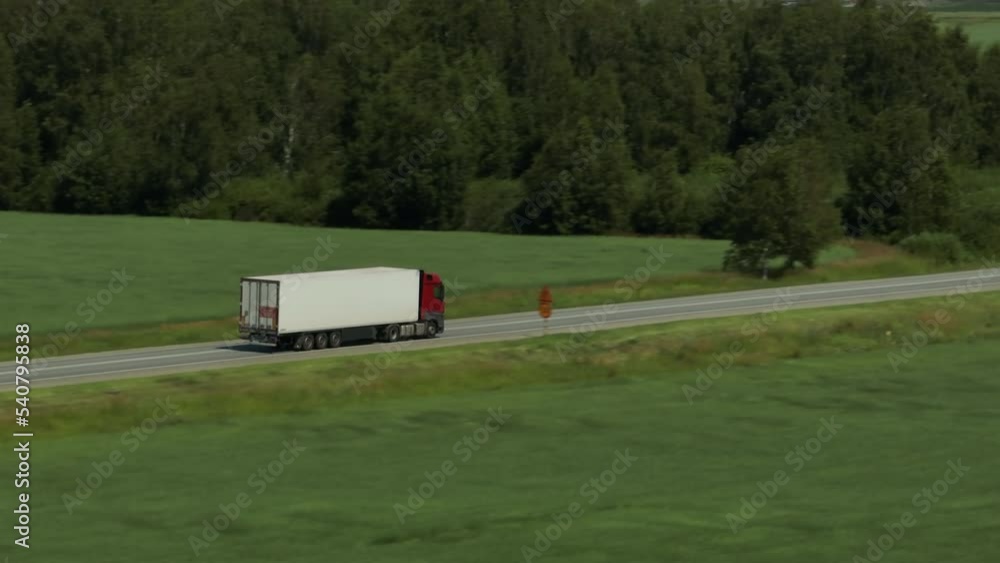 One Semi Truck with white trailer and cab driving, traveling alone on asphalt straight empty road through plain field, highway top down view follow vehicle aerial footage. Freeway trucks traffic One Semi Truck with white trailer and cab driving, traveling alone on asphalt straight empty road through plain field, highway top down view follow vehicle aerial footage. Freeway trucks traffic