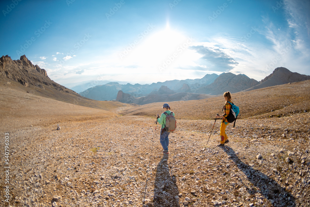 two girls on a walk in the mountains. girls with backpacks walk along a mountain path against the sky.