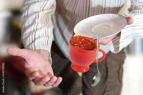 Fotografie A man in sripy shirt dropping teacup with tea, selective focus