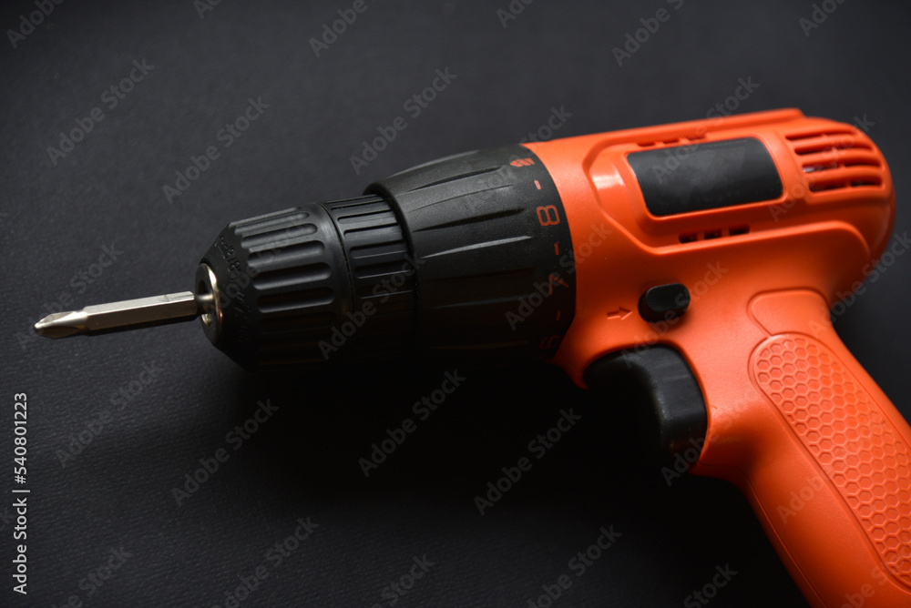 Orange screwdriver on a black background in the hand. Screwdriver and electric drill with power supply