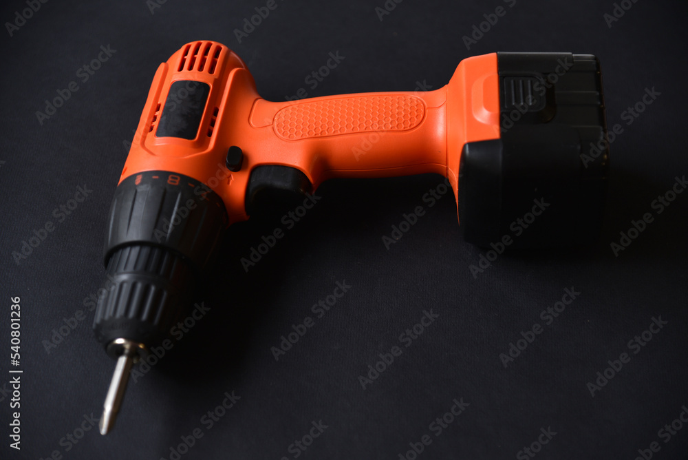 Orange screwdriver on a black background in the hand. Screwdriver and electric drill with power supply Orange screwdriver on a black background in the hand. Screwdriver and electric drill with power supply