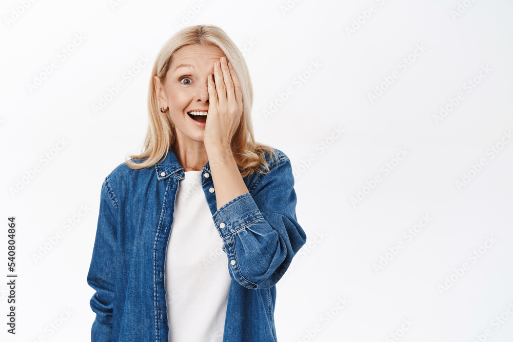 Portrait of beautiful senior woman with blond hair, cover half of face, one side, smiling and looking at camera happy, standing over white background Portrait of beautiful senior woman with blond hair, cover half of face, one side, smiling and looking at camera happy, standing over white background
