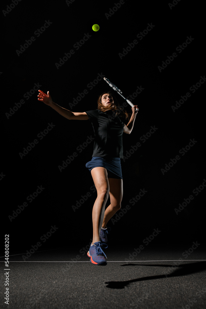 view on female tennis player with tennis racket bouncing to hit yellow tennis ball.