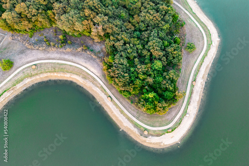 Aerial view of island with green trees and roads surrounded by sea or ocean with clear water. Colorful landscape with beautiful nature. Tourism, traveling.