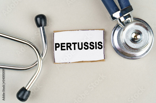 On a gray background, a stethoscope and a cardboard sign with the inscription - Pertussis photo