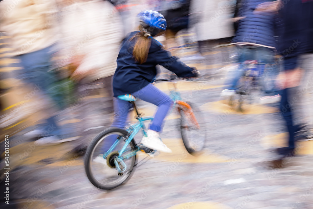 Fototapeta premium motion blur picture of a young unrecognizable girl with a bicycle between crowds of people