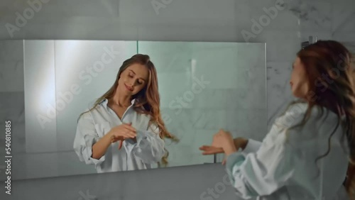 Young beautiful woman in a white shirt applying hand cream in the bathroom.
