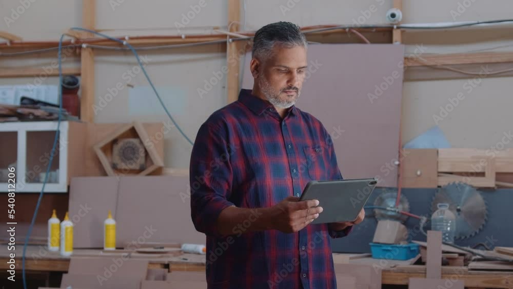 Professional mid adult man scrolling on digital tablet at work in woodworking factory Professional mid adult man scrolling on digital tablet at work in woodworking factory