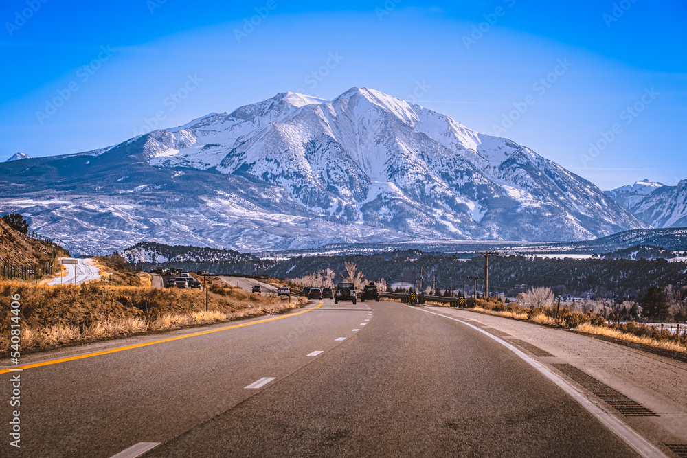View of local Colorado highway leading to beautiful snowcapped mountain - obrazy, fototapety, plakaty 