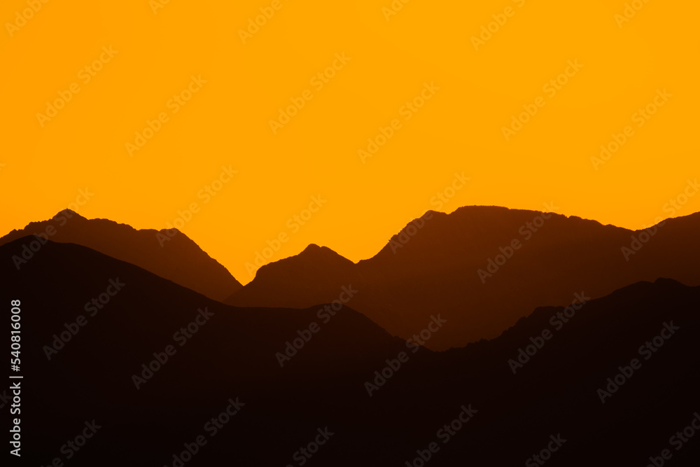 Mountain silhouette landscape at sunset or sunrise with golden hour orange colors. Real mountain silhouettes. Concept of nature, sport, travel, lifestyle.