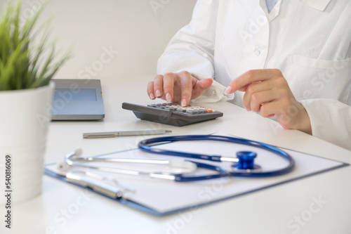 Medical insurance concept . Unrecognizable doctor or nurse with calculator at the table with stethoscope and forms
