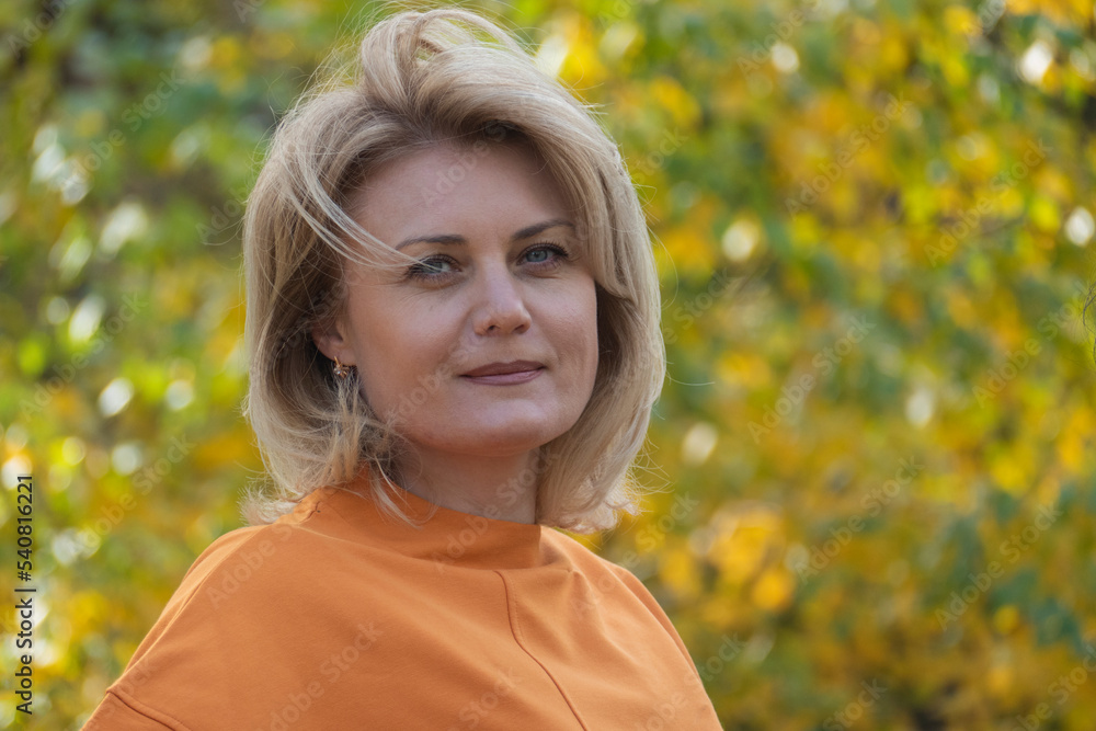 Portrait woman looking at camera in autumn park. Beautiful middle-aged blonde in an orange sweater.Portrait of serious dreamy European lady concentrated somewhere. Blonde Portrait woman looking at camera in autumn park. Beautiful middle-aged blonde in an orange sweater.Portrait of serious dreamy European lady concentrated somewhere. Blonde