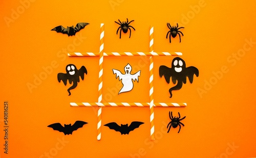 On an orange background, a festive game for Halloween. Figurines symbols of the holiday lie in a row of black spiders, ghosts and bats. The concept of entertainment, the development of thinking.