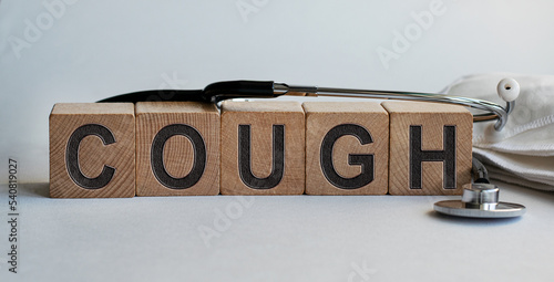 COUGH inscription on wooden cubes isolated on white background, medicine concept. A stethoscope and protective masks are on the table next to it.