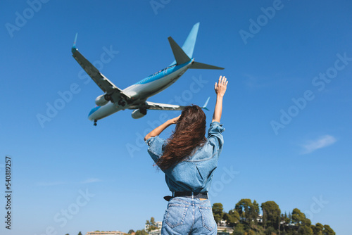 Girl and airplane in flight, landscape with woman standing with hands raised up, waving arms and flying passenger airplane, female tourist and landing commercial aircraft, summer sunny day