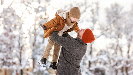 Little son having fun with dad while playing in winter park during New year and Christmas holidays