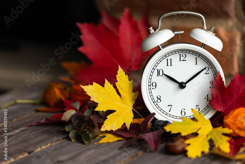 Fall winter time change concept. Autumn composition with retro alarm clock, bright yellow and red leaves, walnut. Brick wall on background. Cozy home atmosphere. Close-up
