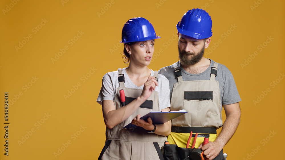 Construction workers calculating measurement on papers, taking notes and planning building process. Wearing helmets and overalls to work on renovation and refurbishment, industrial repair. Construction workers calculating measurement on papers, taking notes and planning building process. Wearing helmets and overalls to work on renovation and refurbishment, industrial repair.