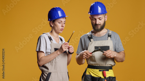 Man and woman builders using screwdriver and wrench to work on construction and industrial rebulding. Team of contractors working with repair tools, holding turnscrew and spanner in studio. photo