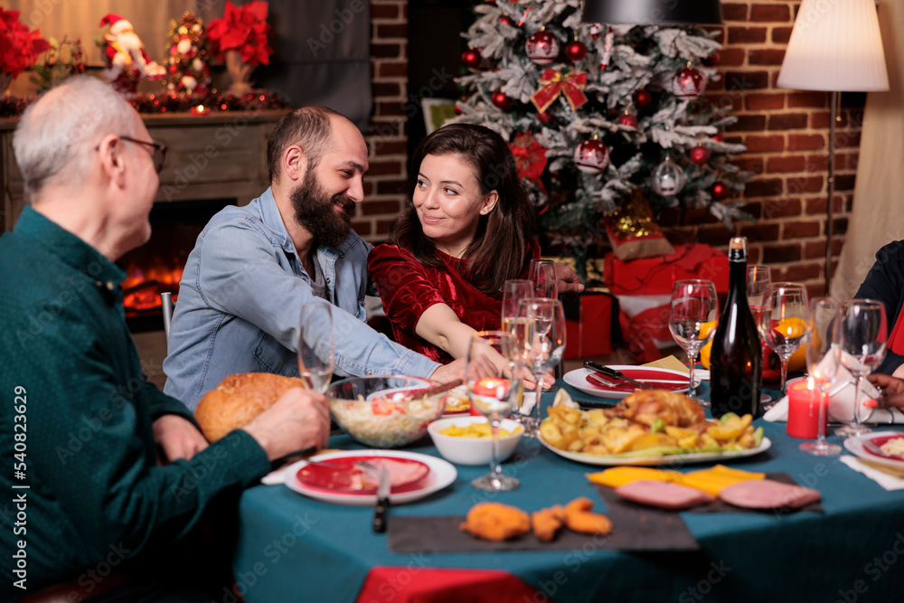 Romantic couple celebrating christmas with family, happy boyfriend and girlfriend talking at festive dinner table. Xmas celebration, wife and husband eating traditional meal with parents Romantic couple celebrating christmas with family, happy boyfriend and girlfriend talking at festive dinner table. Xmas celebration, wife and husband eating traditional meal with parents