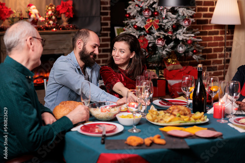 Romantic couple celebrating christmas with family  happy boyfriend and girlfriend talking at festive dinner table. Xmas celebration  wife and husband eating traditional meal with parents