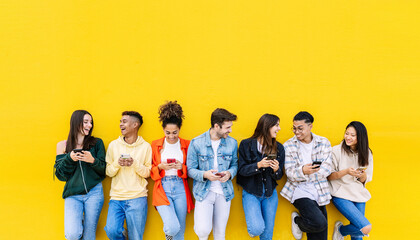 Multiracial young friends having fun sharing media content on mobile phone - Millennial diverse people using smart phone together leaning against wall - Social media trends and technology concept