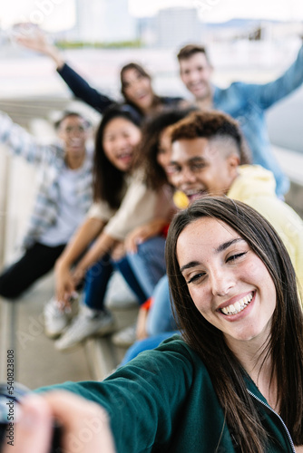 Vertical shot of multiracial young group of friends having fun and laughing while taking a selfie portrait together with camera during vacation - Friendship and travel lifestyle concept