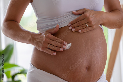 Woman applying cream to dry skin on pregnant belly photo