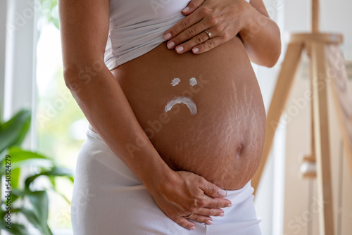 Sad smiley drawn with cream on pregnant belly with stretch marks