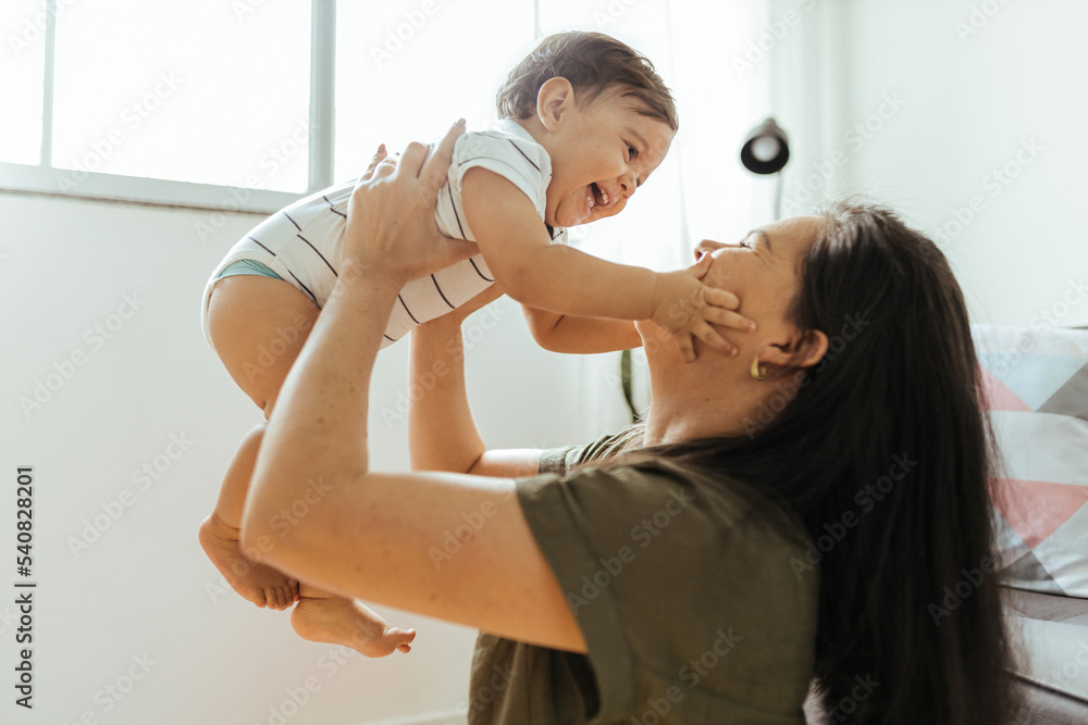 Happy young mother enjoying time with her adorable toddler son at home, lifting him in the air, playing with kid boy in living room Happy young mother enjoying time with her adorable toddler son at home, lifting him in the air, playing with kid boy in living room