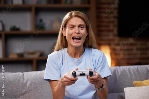 Happy woman using wireless joystick and playing video games at home. Joyful Woman Uses Game Station and Competes in Virtual Games While Resting on Couch