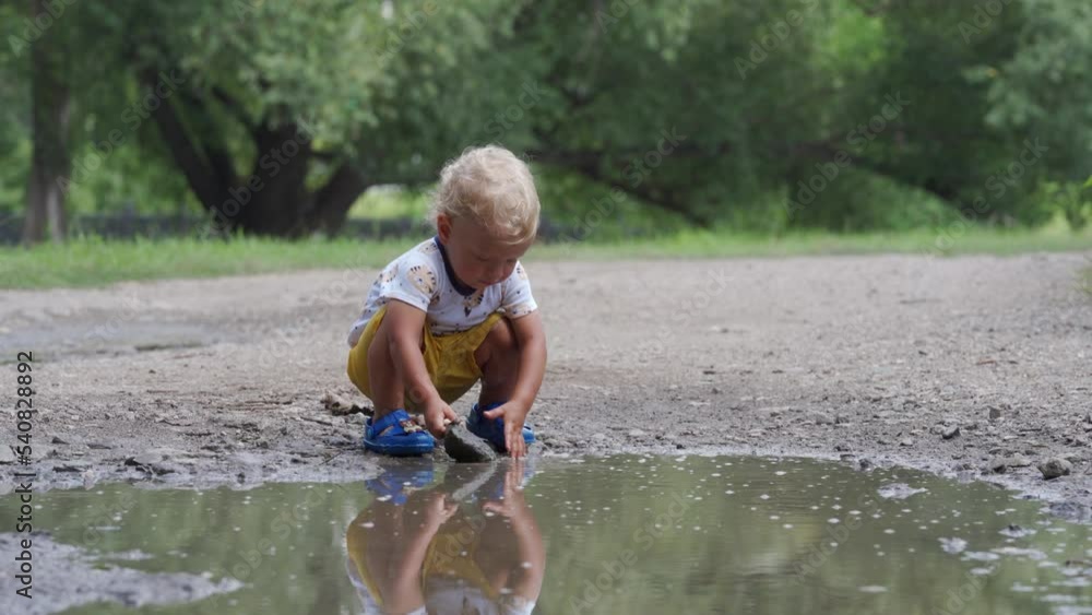 Happy child having fun playing in a puddle of rainwater in summer park. 1.5 year old toddler kid on the nature outdoors. Happy child having fun playing in a puddle of rainwater in summer park. 1.5 year old toddler kid on the nature outdoors.