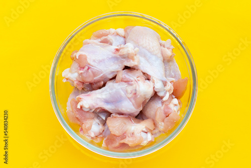 Fresh raw chicken wings (wingstick) in glass bowl on yellow background.