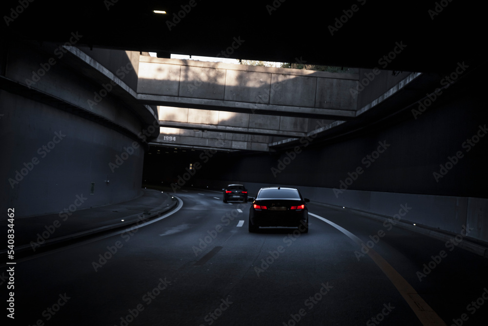 Black car is driving down the road in the tunnel. Traffic infrastructure, tunnel architecture, light effect.