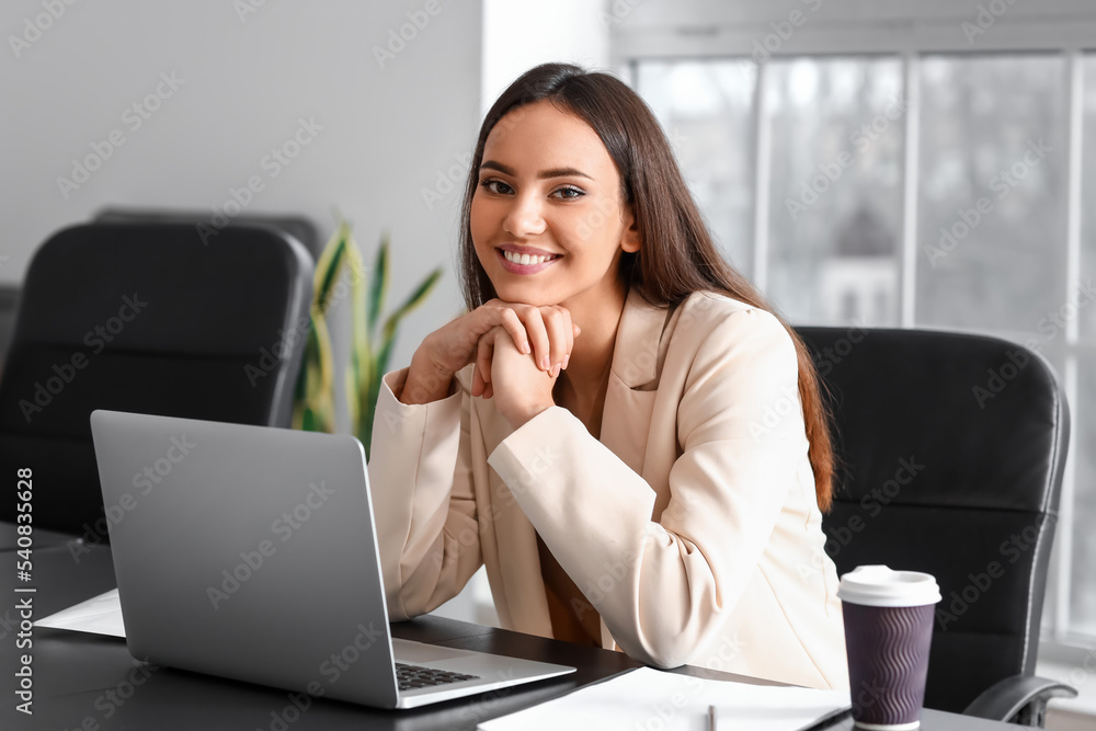 Smiling businesswoman working with laptop at table in office Smiling businesswoman working with laptop at table in office