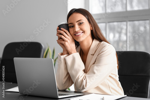 Smiling businesswoman with cup of coffee sitting at table in office