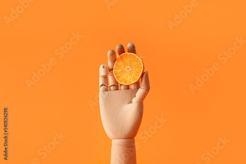 Wooden hand with mandarin slice on orange background
