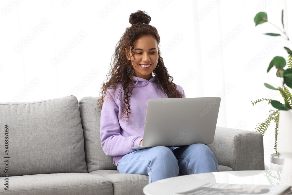 Young African-American woman using laptop on sofa at home Young African-American woman using laptop on sofa at home