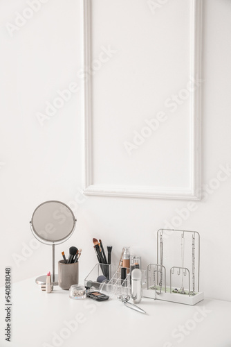 Organizer with decorative cosmetics, makeup brushes, mirror and jewelry on table near light wall