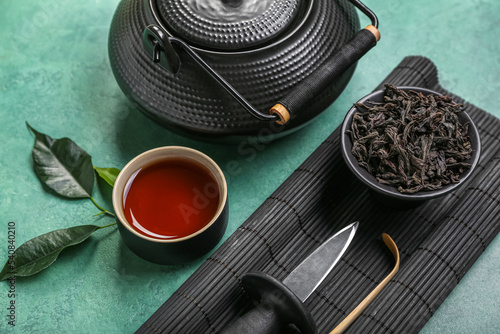 Bamboo mat with bowl of dry puer tea, knife, cup and teapot on grunge background