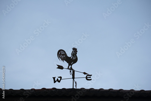 The old wind vane with a rooster symbol icon on the roof, traditional technology equipment for forecast and measuring windy weather in the air, vintage decoration, aiming wind direction instrument. photo