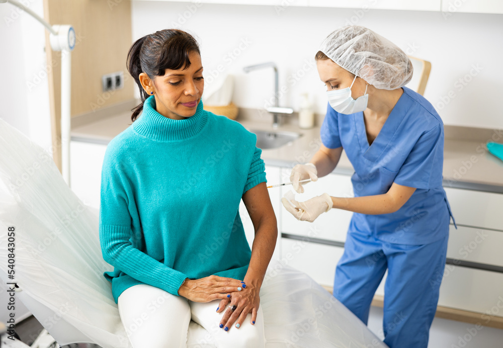 Obraz premium Female doctor in protective face mask vaccinates latino american woman against coronavirus at vaccination center