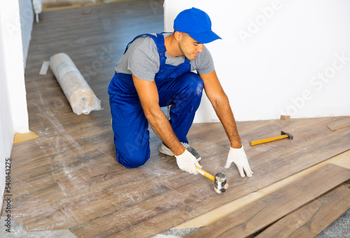Handyman worker in work clothes use rubber hammers installing laminate panel in apartment, home repair