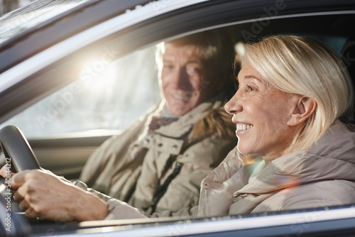 Side view portrait of cheerful senior couple driving car in winter, focus on smiling woman behind wheel, copy space