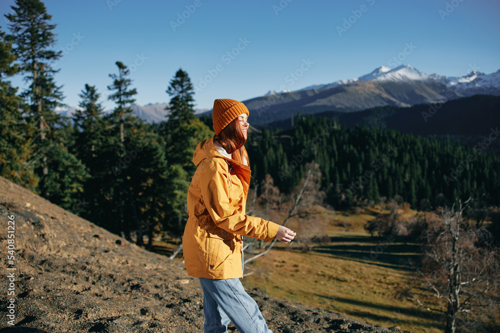 Woman full back hiker running on the mountain looking at nature happiness overlooking snowy mountains and trees in yellow raincoat travel and hiking in the mountains at sunset freedom
