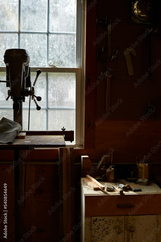 Drill press and wood working tools on table in front of a window. Natural lighting in artist's studio. 