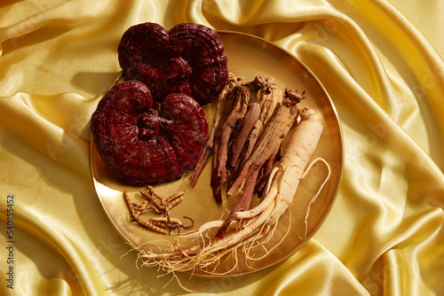 A gold tray with cordyceps, ginseng, and Ganoderma lucidum displayed on a background of gold silk.