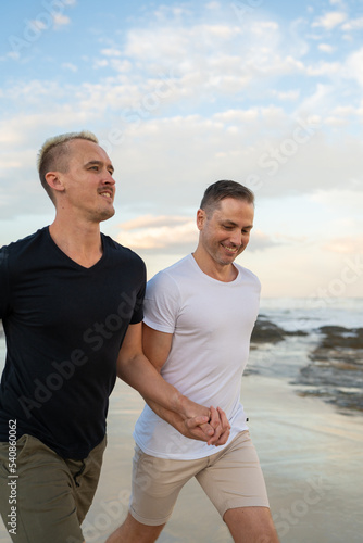 gay couple running together holding hands on beach smiling